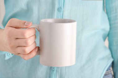 Reklam mesajınız ya da tanıtım içeriğiniz için boş fotokopi alanı olan beyaz bardağı tutan kadın. Mavi gömlekli kız elinde beyaz porselen kahve ya da çay fincanı tutuyor.