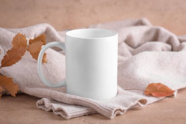 Reklam mesajın için boş fotokopi alanı olan beyaz kupa mı yoksa sonbahar yapraklı bej kazak içeriği için tanıtım içeriği mi? Bej taşlı arka planda porselen kahve fincanı.