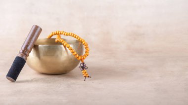 Çubuklu Tibet şarkı kasesi, bej taşlı arka planda mantra meditasyonlarda kullanılan mala boncukları. Meditasyon, rahatlama, yoga, masaj ve akıl sağlığı için müzik aletleri