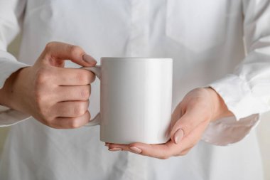 Reklam mesajınız ya da tanıtım içeriğiniz için boş fotokopi alanı olan beyaz bardaklı kadın eli. Beyaz gömlekli kız elinde beyaz porselen kahve fincanı tutuyor.