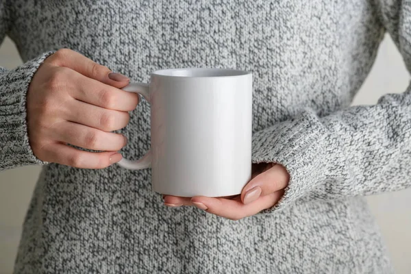 Female hands holding white mug mockup with blank copy space for your advertising text message or promotional content. Girl in grey sweater holding white porcelain coffee mug mock up, close up