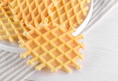 Ferratelle ya da pizzelle geleneksel bir tatlı ya da beyaz ahşap arka planda bir tabakta kurabiyeler, yakın plan. İtalya, Abruzzo 'nun bölgesel mutfağı. Meşhur waffle gibi.