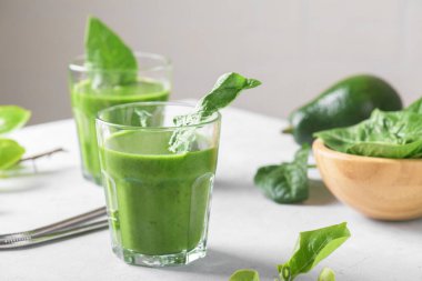 Ispanak, avokado, muz ve vejetaryen sütlü sağlıklı yeşil smoothie ve açık gri masa arkaplanında taze malzemeler. Detoks, diyet, sağlıklı, vejetaryen gıda konsepti