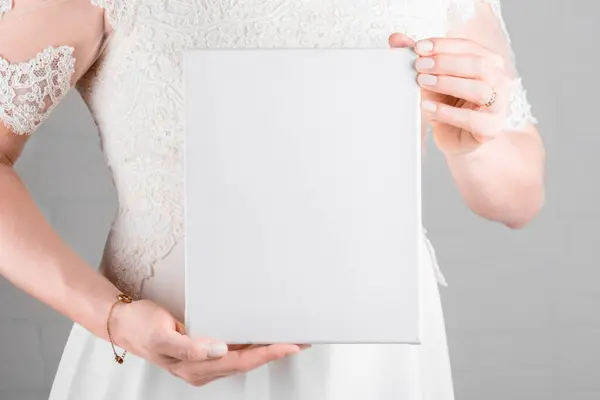 Bride holding white canvas mockup on white wall background. Minimal stile blank mockup, picture mockup, template canvas mockup for art work or presentation your design