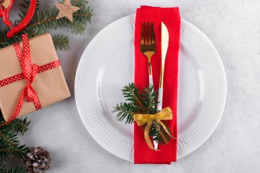 Doğal köknar dalları, Noel hediyesi ve açık gri masa zemininde altın çatal bıçak seti olan güzel bir Noel masası. Noel yemeği için şenlikli dekorasyon, düz yatak, üst manzara