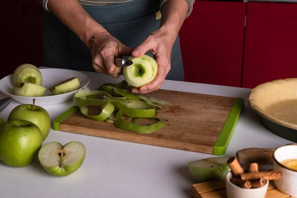 Woman is peeling apples to prepare apple pie in the kitchen. Authentic female hands peel an apple with a knife. Cooking apple pie process, recipe step by step. Thanksgiving fruit tart, autumn bakery