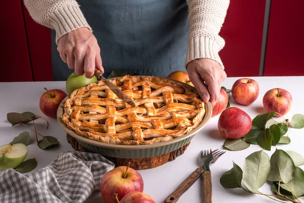 Woman cutting a baked apple with a khife, Thanksgiving traditional dessert ready to eat with red and green apples, Thanksgiving tart preparation, autumn bakery. Crispy weather sweets. Recipe