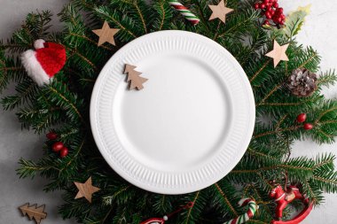 Doğal köknar dallarının arka planında beyaz seramik tabakla Noel sofrası. Noel yemeği, düz yatak, üst manzara, tebrik kartı şablonu için Noel ziyafeti