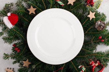Doğal köknar dallarının arka planında beyaz seramik tabakla Noel sofrası. Noel yemeği, düz yatak, üst manzara, tebrik kartı şablonu için Noel ziyafeti