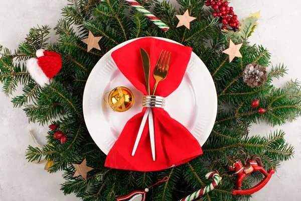 Christmas table setting with gold cutlery and red napkin on white plate on natural fir branches background. Christmas festive decoration serving for Christmas dinner, flat lay, top view