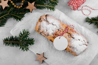 Hediye etiketi ile süslenmiş Noel, geleneksel Alman ekmeği, doğal köknar dallı açık gri arka planda bayram pastası tatlısıdır. Manzara, Noel yemekleri düzdü.