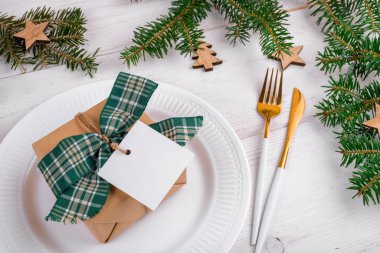 Hediye kutusuyla Noel sofrası, beyaz tabakta kare şeklinde maket, altın keski, doğal köknar dalları, Noel süslemeleri, üst manzara. Tatil kış kompozisyonu, kopyalama alanı