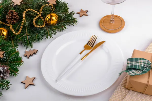 stock image Christmas table setting with gold cutlery and white ceramic plate on light gray table background with natural green fir. Golden festive decoration for Christmas dinner, flat lay, top view