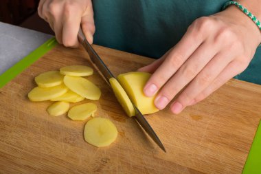 Hakiki kadın elleri mutfak masasında tahta kesme tahtasıyla patates kesiyor. Önlüklü kadın patates kesiyor, yemek hazırlıyor, evin içini, ev hayatını, yaşam tarzını. Kapat.