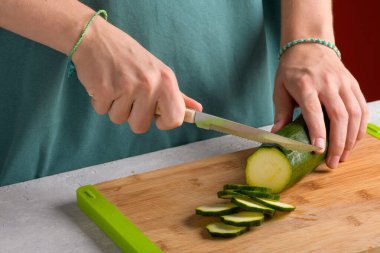 Hakiki kadın elleri mutfak masasında tahta kesme tahtasıyla kabak kesiyor. Önlüklü kadın yemek hazırlamak için kabak kesti. Vejetaryen ve vejetaryen yemek tarifi, mutfak. Ev hayatı, yaşam tarzı.