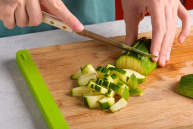 Hakiki kadın elleri mutfak masasında tahta kesme tahtasıyla kabak küp kesiyor, kapat. Vejetaryen ve vejetaryen yemekleri, vejetaryen yemekleri. Ev hayatı, yaşam tarzı.
