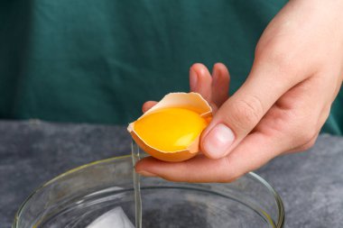 Yumurta kabuklarını sarıyla tutan eller, yaklaşın. Ev hanımı elleri yumurta sarısını ve beyazı cam bir kaseye ayırır. Yemek pişirme süreci, yakın çekim.