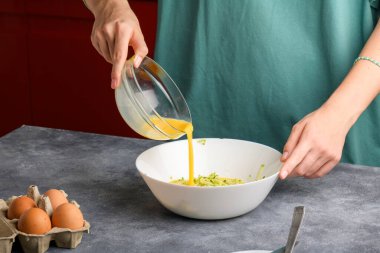 Kadın elleri rendelenmiş kabakla omlet pişirirken, rendelenmiş kabaklı bir kaseye çırpılmış yumurta ekler. Kahvaltı için çırpılmış yumurta ve kabak pişiriyorum.