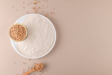 Seramik tabakta karabuğday unu ve bej renkli arka planda çiğ karabuğday tohumu, üst manzara, kopyalama alanı. Alternatif un, glütensiz un, sağlıklı beslenme.