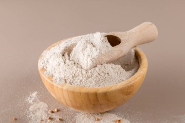 Tahta bir kasede karabuğday unu ve bej renkli tek renkli arka planda çiğ karabuğday tanesi. Alternatif un, glütensiz un, sağlıklı beslenme.
