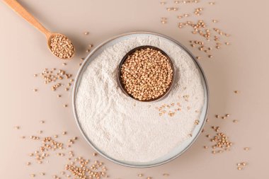 Seramik tabakta karabuğday unu ve bej renkli tek renkli arka planda çiğ karabuğday tohumu, üst manzara. Alternatif un, glütensiz un, sağlıklı beslenme.