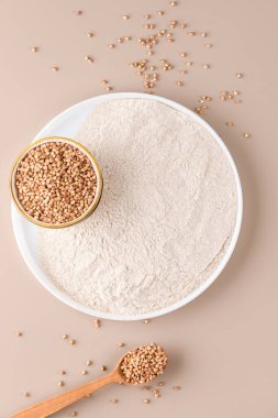 Seramik tabakta karabuğday unu ve bej renkli tek renkli arka planda çiğ karabuğday tohumu, üst manzara. Alternatif un, glütensiz un, sağlıklı beslenme.