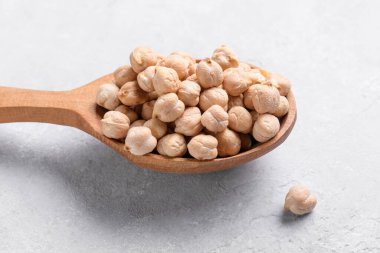 Ahşap kaşıkta çiğ nohut ve gri masa arkaplanı. Sağlıklı ve doğal vejetaryen yemekleri.