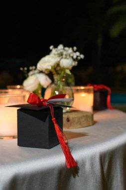 Mezuniyet partisi konsepti. Mum ışığında kırmızı kurdeleli siyah kare akademik şapka.