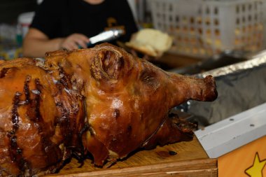 Canlı bir açık hava yemek etkinliğinde bütün bir kızarmış domuz. Bir yiyecek satıcısı arka planda bir sandviç hazırladı, neşe ve kutlamalarla dolu hareketli bir atmosferi vurguluyordu.