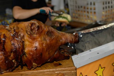 Canlı bir açık hava yemek etkinliğinde bütün bir kızarmış domuz. Bir yiyecek satıcısı arka planda bir sandviç hazırladı, neşe ve kutlamalarla dolu hareketli bir atmosferi vurguluyordu.