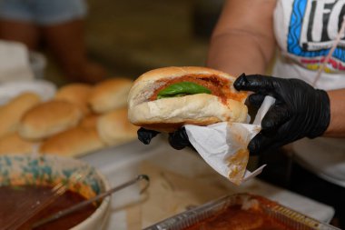 Bir satıcı, akşam yerel bir yemek festivali sırasında taze fesleğenle kaplanmış domates soslu yeni yapılmış bir sandviç servis ediyor.