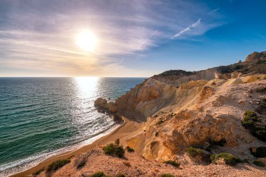 Güneşli bir akşamda tenha ve uzak plajların güzel alçak güneş manzarası. Yüksek sarı uçurumlar, yıpranmış kayalar, gök mavisi deniz suları, kumlu sahil, açık gökyüzü, insan yok. Agios Ioannis Sahili ve Ege Denizi