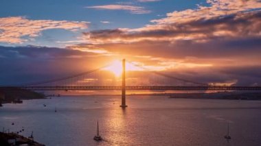 25 Nisan 'da Lizbon, Portekiz Köprüsü üzerinde güzel bir günbatımı zamanı. Ünlü bir dönüm noktası, güneşin altında renkli bir zaman çizgisi, Tagus ya da Tejo nehrinde gidip gelen yelkenliler, arabalar ve trenler