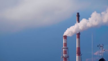 İki yığın birleşik ısı ve elektrik santrali mavi gökyüzüne beyaz duman yayıyor. Rüzgarda bir yığın beyaz duman sallanıyor. Isıtma, ısı üretimi, enerji krizi, çevre sorunları, hava kalitesi