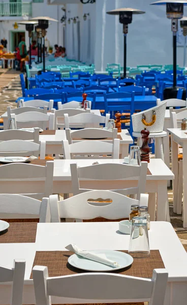 stock image Colorful tables and chairs, whitewashed walls of restaurants, cafes and bars in Naoussa bay, on sunny summer day. Traditional Greek cuisine, vacations, travel destination, tourist paradise, selective