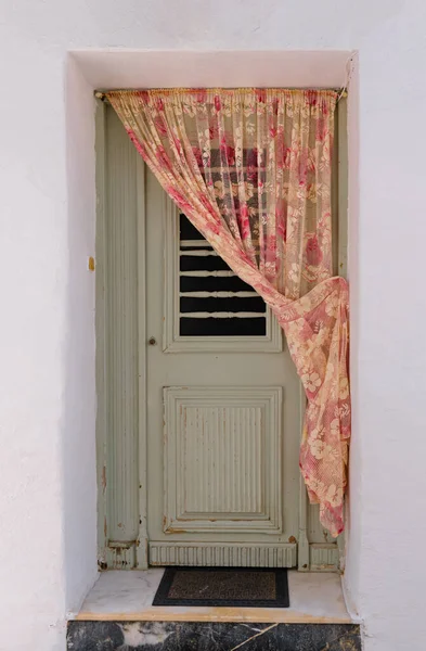 Frontal shot of authentic doorway of traditional Greek house, whitewashed walls, curtains, vintage wood, weathered door. Typical local architecture of the Cyclades islands, Paros island, Greece
