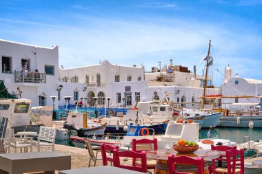 Naoussa Körfezi 'nin kıyısındaki deniz ürünleri restoranları, kafeler ve barlar masalarla demirlenmiş balıkçı tekneleri. Geleneksel Yunan mutfağı, beyazlatılmış evler ve kilise, kıyı şeridinde renkli masa ve sandalyeler