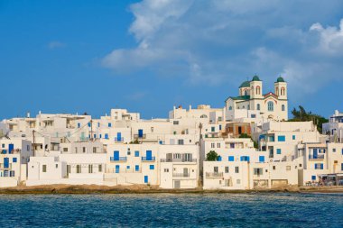 Yunanistan 'ın güneşli bir günde, Naoussa, Paros Adası, Yunanistan' da, deniz kenarındaki evleri beyazlatan geleneksel Yunan evleri. Tepenin tepesindeki Dormition of Mother of God Kilisesi, açık mavi gökyüzü, yaz güneşi