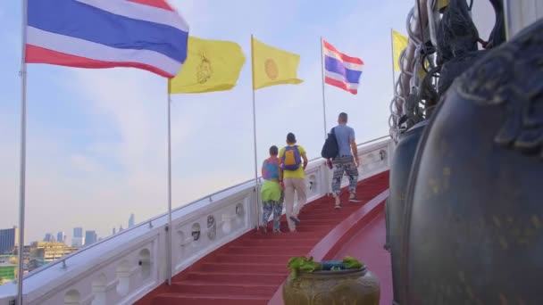 観光客はワット サケや黄金の山の寺院の赤い階段を登る 赤い階段と白いパラペットの螺旋階段に沿ってタイの国家 タイ王室の旗の行 前景がぼやけて鐘 — ストック動画