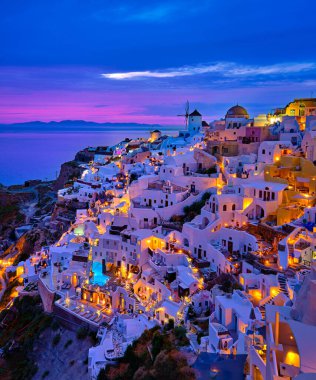 Yunanistan 'ın gün batımında, Santorini Adası' nda geleneksel bembeyaz evleri ve yel değirmenleriyle Oia köyünün güzel manzarası. Manzaralı seyahat arka planı, ünlü hedef, renkli gökyüzü ve bulutlar. 