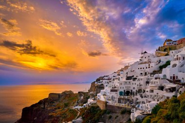 Yunanistan 'ın gün batımında, Santorini Adası' nda geleneksel bembeyaz evleri ve yel değirmenleriyle Oia köyünün güzel manzarası. Manzaralı seyahat arka planı, ünlü hedef, renkli gökyüzü ve bulutlar. 