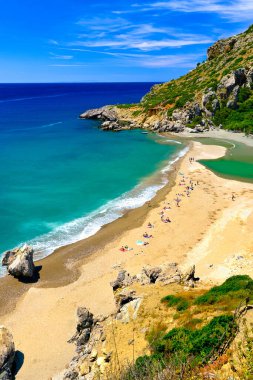 Yunanistan 'ın Preveli, Girit Adası' ndaki kumlu sahil manzarası güneşli bir günde. Seyahat güzergahı, nehir ve berrak Libya deniz suları, orman, palmiye ağaçları, vadi, bulutlu mavi gökyüzü. Turist yüzüşü ve