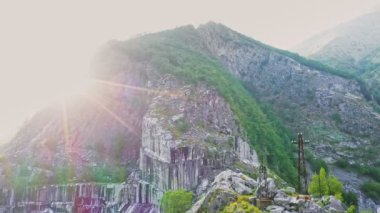 İHA 'nın hava atışı, terk edilmiş mermer ocağının yüksek kayası, Apuan Alps dağları, Carrara, İtalya' ya doğru yavaşça iniyor. Çürümüş kaya ve endüstriyel atıklar, parlak güneş ışığı, güneş ışınları ve parlayan güneş.