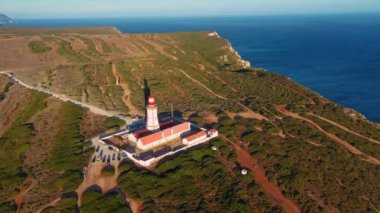 Güneş batarken Cabo Espichel ya da Cape Espichel 'deki deniz fenerinin insansız hava aracı görüntüsüne yaklaş. Atlantik Okyanusu kıyısı, Sesimbra, Portekiz. Yaklaş, doli, yüksek uçurumlar, Portekiz mimarisi