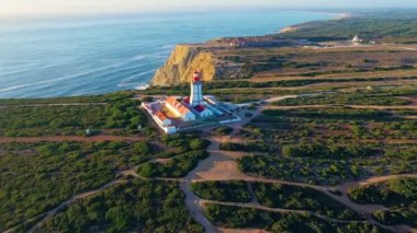 Gün batımında Cabo Espichel ya da Cape Espichel 'deki deniz fenerinin insansız hava aracı görüntüsüne yaklaşıyoruz. Atlantik Okyanusu kıyısı, Sesimbra, Portekiz. Çek, yüksek uçurumlar, Portekiz mimarisi, günbatımı yazı.