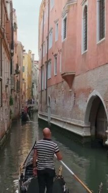 Gondol, İtalya 'da Venedik' te, gündüz vakti dar sularda veya Rio 'da iniyor. Gondolcu seyir teknesi. Turistler gezintiden zevk alıyor, fotoğraf çekiyorlar. Ortaçağ binaları, kanal suları. 4k görüntü, tanımlanamaz.