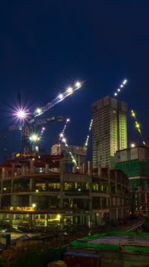 Dikey zaman çizelgesi, inşaat alanının gece görüntüleri. Dramatik bulutlar, birçok vinç hareket ediyor modern şehrin ortasındaki yüksek binalar, parlak ışıklar parlıyor. Kentleşme, gelişme. Kuala Lumpur