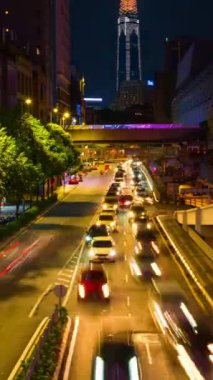 Modern Asya şehir sokağının geceleri dikey zaman çizelgesi. Az ışık, az ışık. Trafik ışıkları, parlak şehir ışıkları, reklamlar, insanlar caddeleri geçiyor, trafik sıkışıklığı, arka planda gökdelen. Yol ayrımında