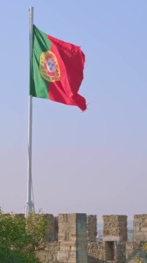 Low sun view of national flag of Portugal waving in the wind on a clear sunny day at blue sky over olive trees of Castelo de Sao Jorge. Patriotism, democracy, politics, nation, European union member