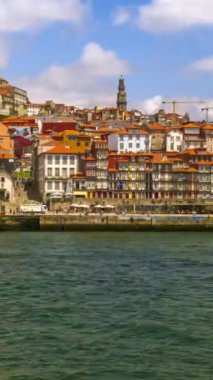 Day time lapse of clouds fly above Portos oldest district Ribeira by Douro river, Portugal. People rush around embankment, tourist boats rush up and down, river taxi crossing Douro. Summer sunshine